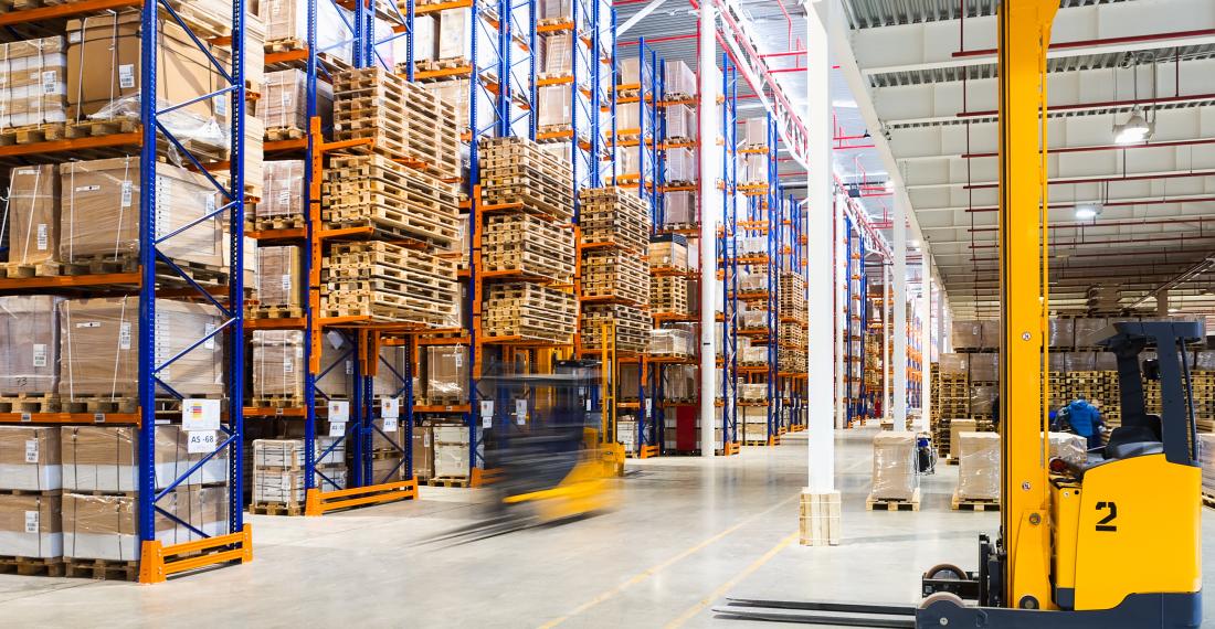 Warehouse with machinery and shelves full of boxes and palettes.